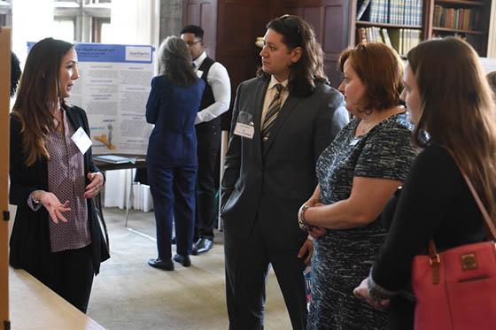 Photo of a Chatham University student standing in front of a poster board, presenting to peers